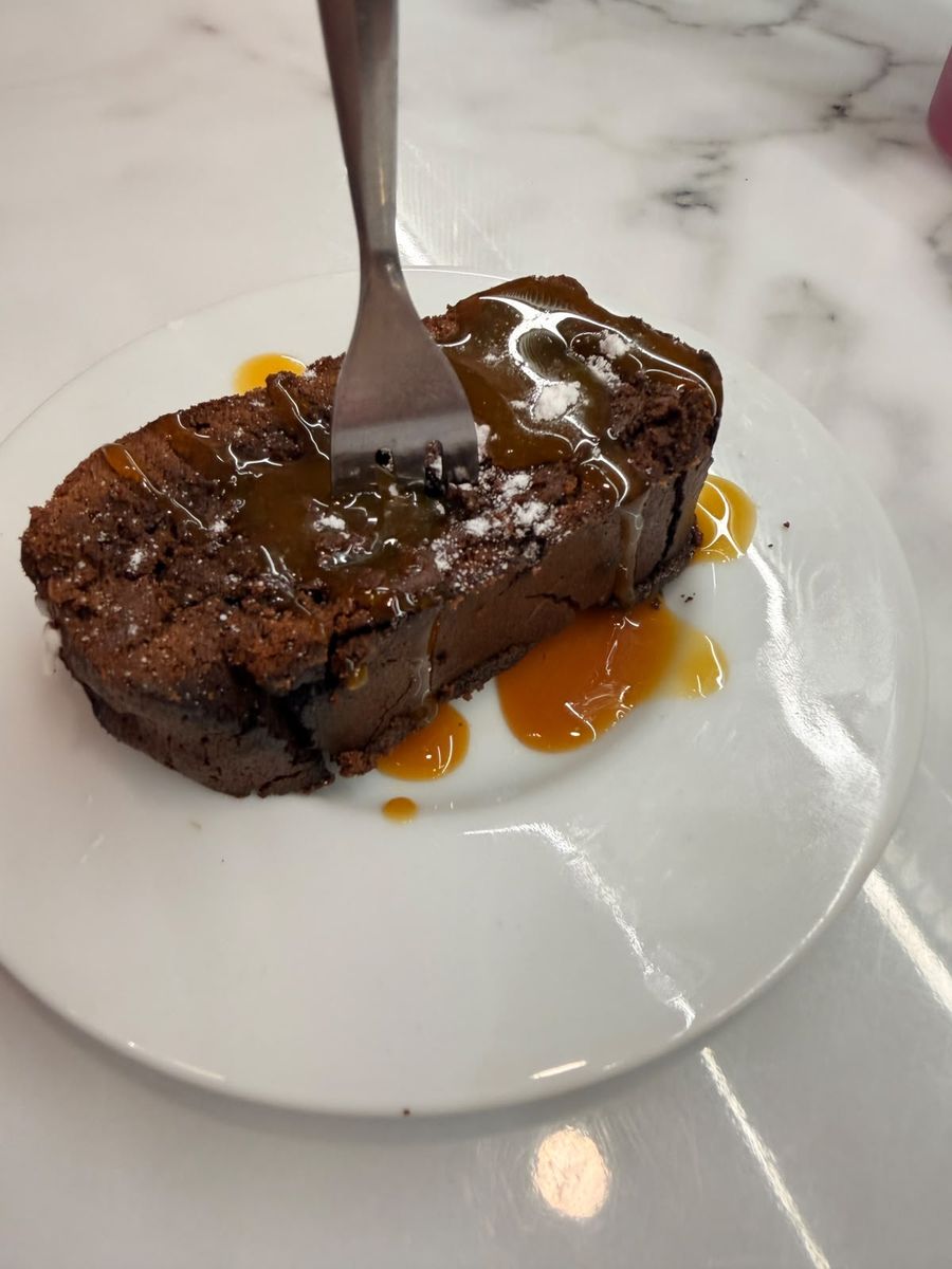 Chocolate brownie with caramel drizzle and icing sugar, fork at the ready — fudgy and made fresh at Hora Mansa.